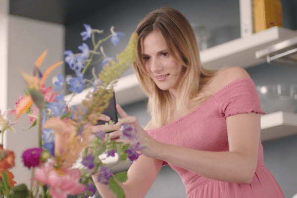Woman in pink dress taking a picture of flowers for Bloomon
