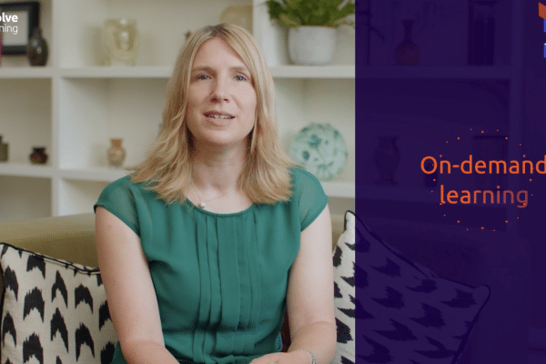 A lady sat on a sofa in a green dress talking to camera with motion graphics to her right