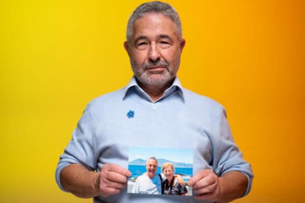 A man in his 60s wearing a blue shirt holding a family photo