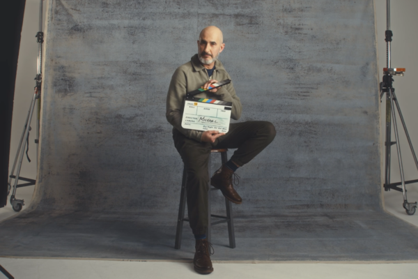 Bald man sat on a stool in a studio with a clapperboard