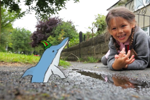 Young girl laughing on the sidewalk looking at an animation of a dolphin