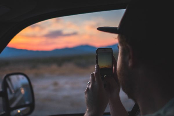 Man taking a picture of the sunset from his car window