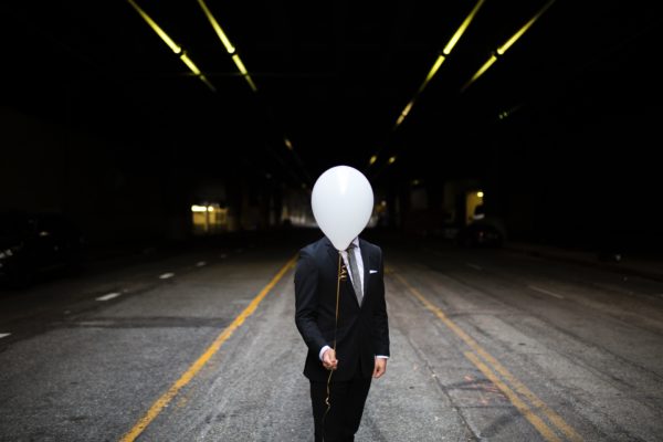Man dressed smarty holding a white balloon in front of his face in the street