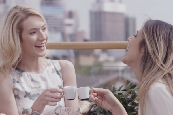 Two women laughing while clinking two small cups with espresso