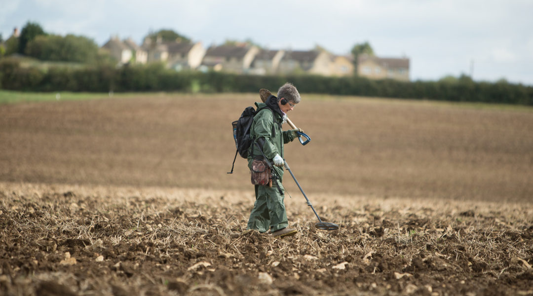 Woman using a metal detector in a field