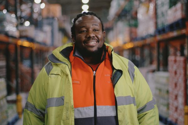 black man in a high viz jacket in a warehouse smiling