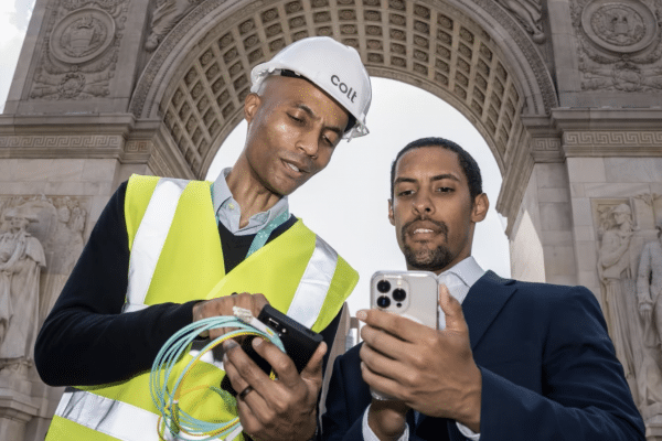 man in high viz jacket and hard hat holding cable with a man using his phone taken from a low angle